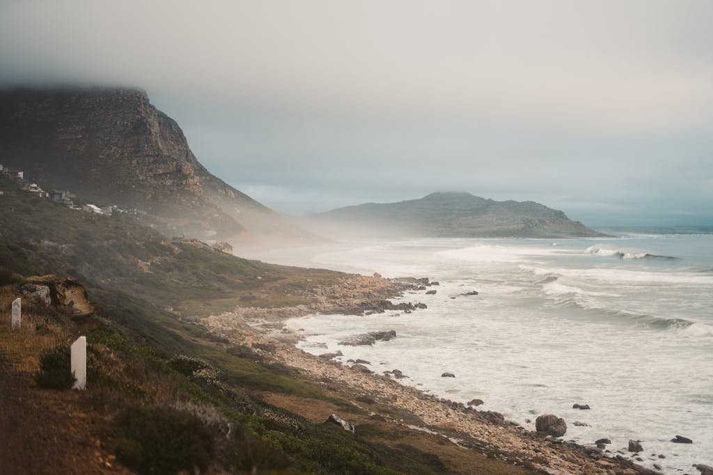 A serene view of Cape Town's coastline with misty cliffs and crashing waves.