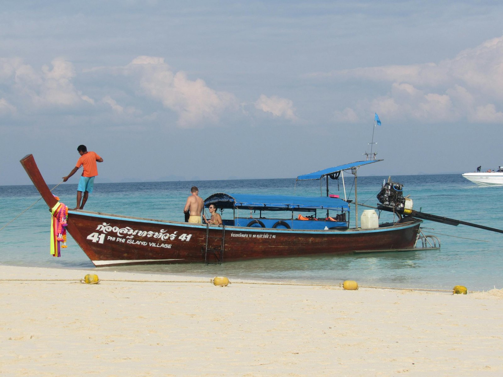 A vibrant long-tail boat on a sandy beach at Phi Phi Island, Thailand, under a clear blue sky.